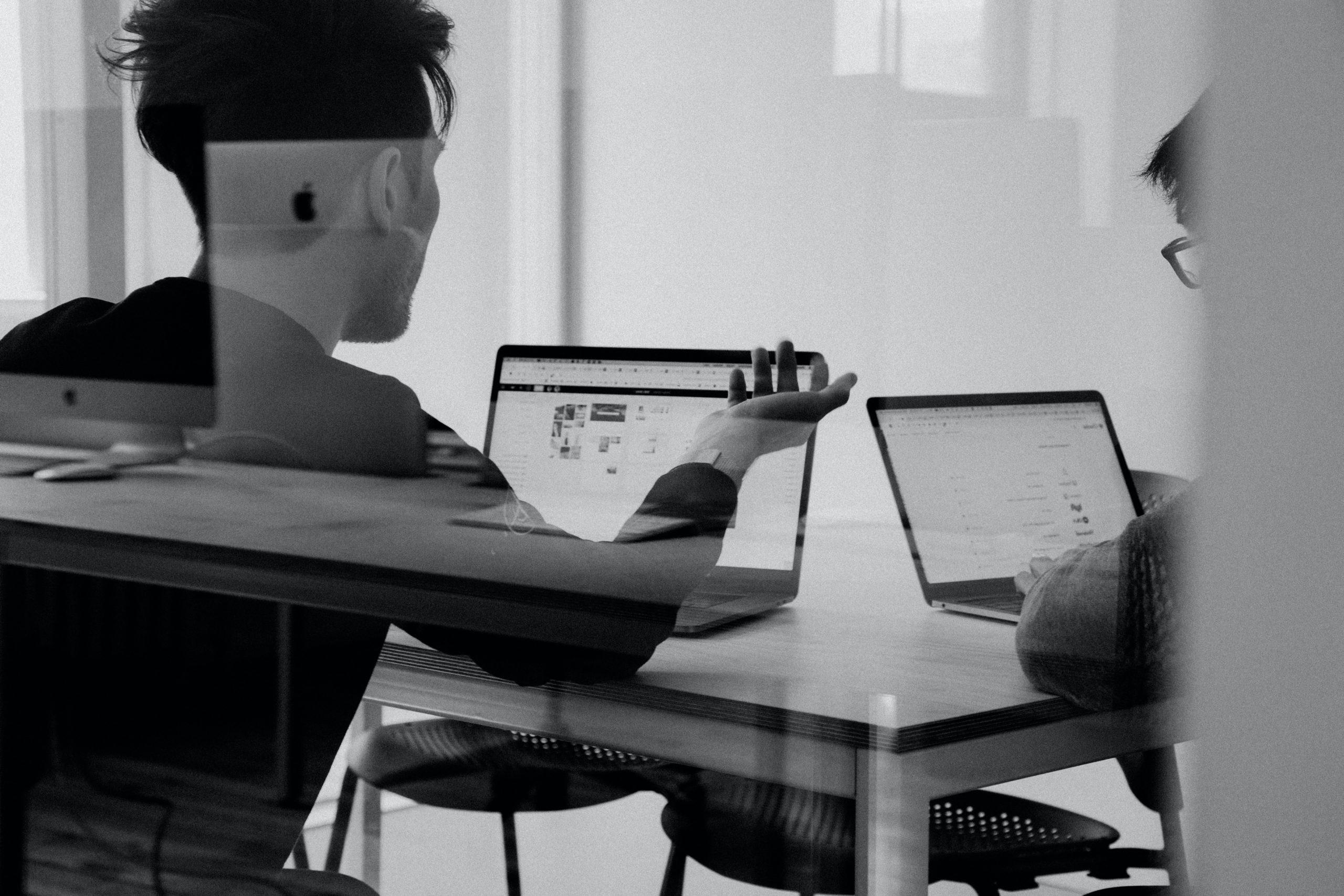 两个人坐在一张桌子旁，用笔记本电脑聊天