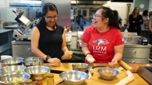 索菲娅·特兰和斯蒂芬妮·李示范了如何制作momos, 一种受欢迎的尼泊尔饺子, 在酒店厨房学院最近的一次研讨会上. 在这里，两人都笑着哄骗, 当他们包饺子的时候，面前摆着一堆菜.