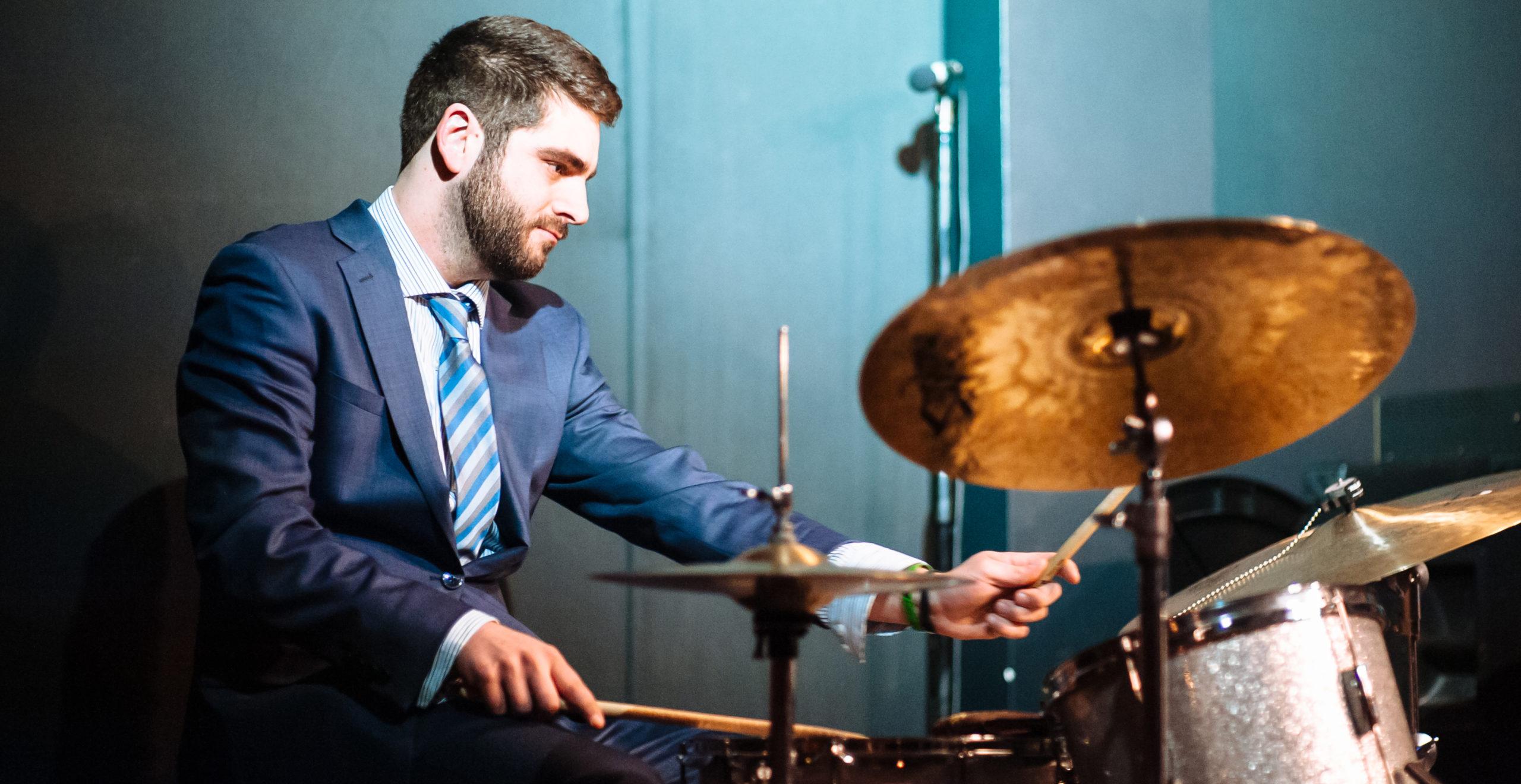A drummer in a suit performing in a green room